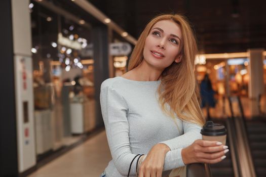 Attractive young woman looking away dreamily, enjoying her coffee while shopping at the mall