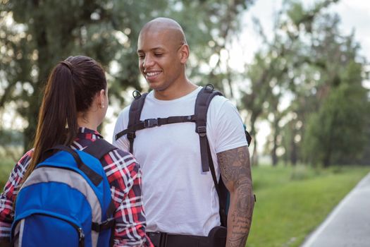 Cheerful handsome African man with backpack talking to his girlfriend on countryside road, copy space. Lovely couple travelling together, hitchhiking on the road