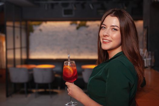 Happy beautiful young woman smiling to the camera while having a drink at the bar