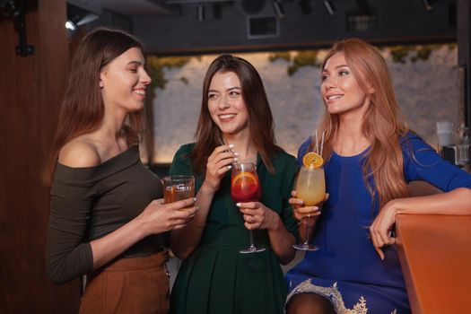 Group of three beautiful young women chatting over drinks at the bar. Female friends enjoying celebration at the restaurant
