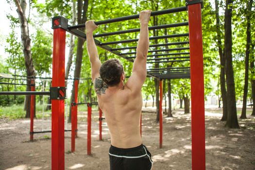 Rear view shot of a sportsman exercising on calistenics park playground outdoors