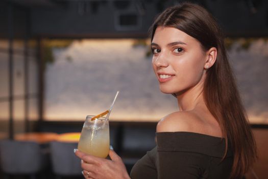 Close up of a beautiful young woman smiling over her shoulder to the camera, enjoying a drink at the bar