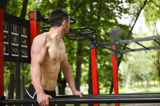 Strong muscular shirtless man working out on calisthenics workout equipment outdoors, copy space