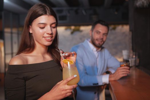 Beautiful young woman having a drink at the bar, handsome man smiling at her seductively. Dating, love, seduction concept