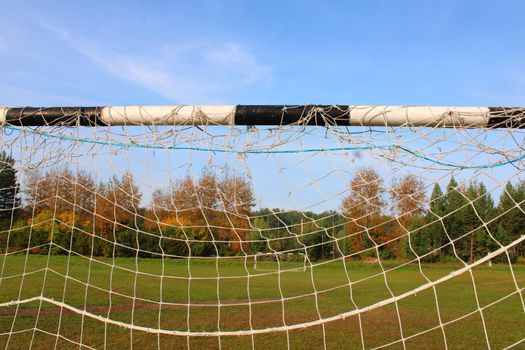 Old football goal against the background of the football field and autumn forest