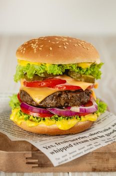 Delicious burger with meat, melted cheese, dripping sauce and vegetables on white rustic background. Freshly made tasty hamburger, close-up.