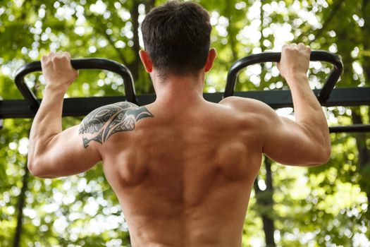 Rear view shot of a shirtless strong muscular man doing pull ups