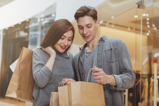 Beautiful young couple examining their purchase, looking inside shopping bags, enjoying spree at the mall. Consumerism, fashion, buying concept