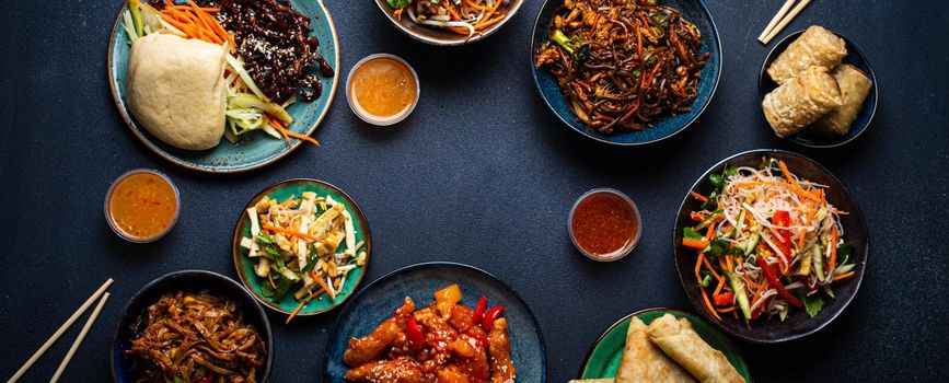 Set of Chinese dishes on table: sweet and sour chicken, fried spring rolls, noodles, rice, steamed buns with bbq glazed pork, Asian style banquet or buffet, top view with copy space.