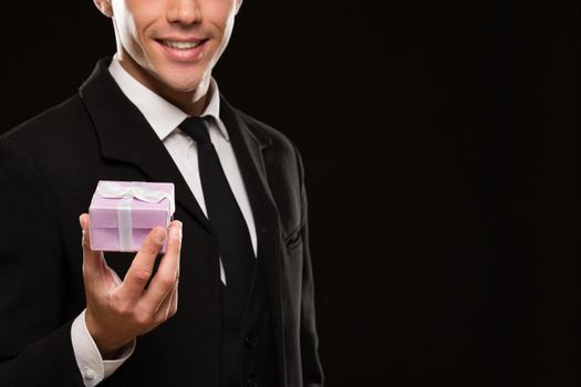 Cropped shot of an attractive suited man holding out a gift with a bow to the camera smiling seductively on black background copyspace love romance relationships dating valentines surprise