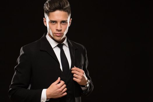 Attractive young macho man bodyguard suiting up on black background copyspace confidence success tension aggressive masculine powerful businessman serious seductive secret agent