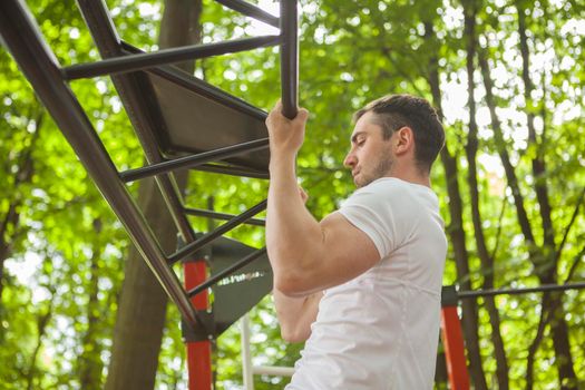 Low angle profile shot of a sportsman doing pull ups outdoors