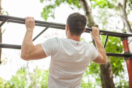 Rear view shot of a male athlete doing pull ups, working out outdoors
