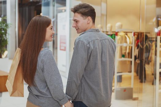 Rear view shot of a young happy couple smiling at each other, enjoying shopping at the mall together. Consumerism, love, seasonal sales concept