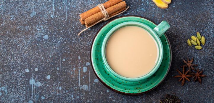 Healthy Indian beverage masala chai - tea hot drink with milk and spices in rustic green teacup with ingredients for making masala chai from above on concrete blue background copy space