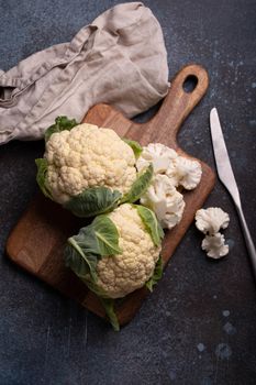 Fresh organic cut cauliflower on wooden cutting board with kitchen knife, ready to be cooked, top view with copy space. Vegetarian food, clean eating concept .