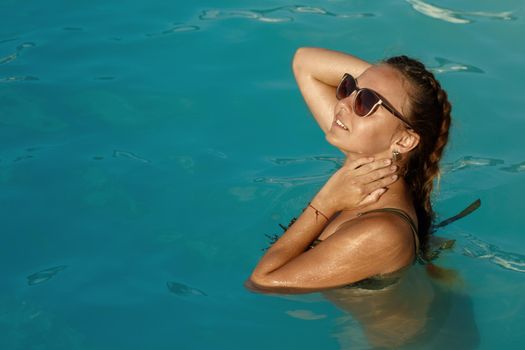 Shot of a stunning beautiful young tanned woman enjoying swimming in the pool at the hotel. Happy woman smiling while relaxing in the pool, copy space. Recreation, summer, tourism, lifestyle concept