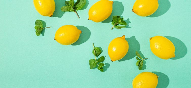 Fresh yellow lemons with mint on minimal blue background on bright sun light with hard shadows pattern summer background flat lay from above, citrus food composition, space for text