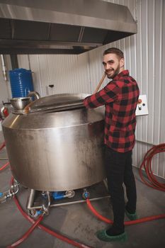 Cheerful brewer smiling to the camera while controlling beer fermentation process at his microbrewery