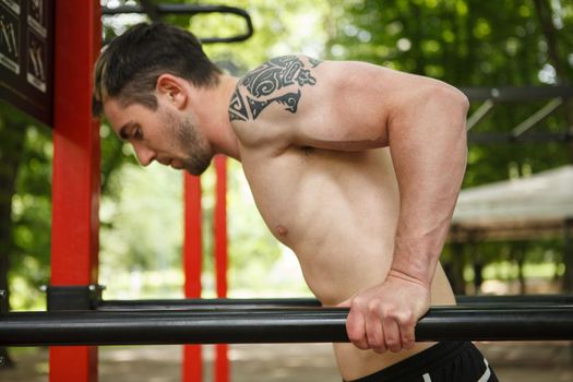 Close up of a handsome sportsman doing triceps dips on calisthenics playground