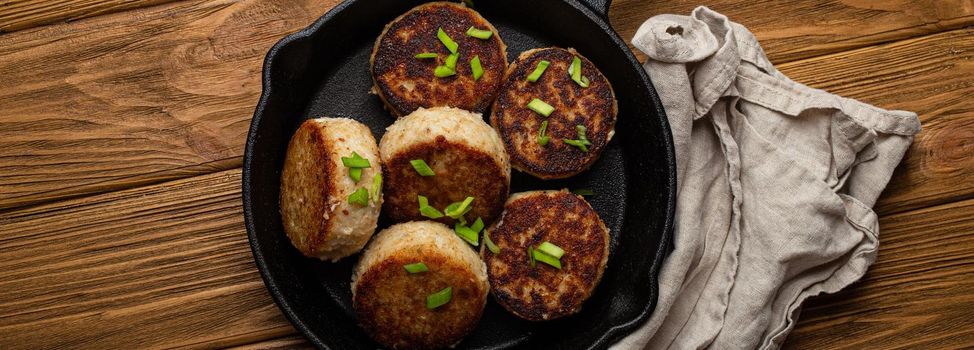 Homemade cutlets from fish, chicken or meat on black cast iron frying pan skillet on rustic wooden table, traditional meal roasted healthy cutlets in pan from above