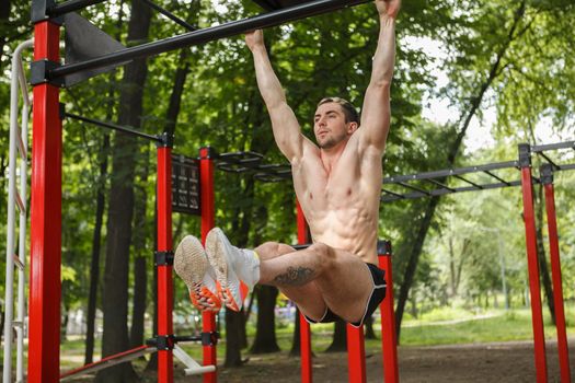 Ripped handsome sportsman exercising outdoors, doing toes to bar abs workout