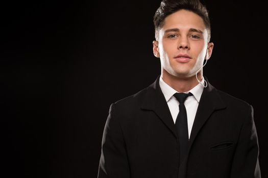 Close up studio portrait of a handsome confident young secret agent looking to the camera seriously on black background suit fearless bravery guarding FBI police safety focused ready