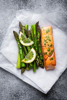 Grilled salmon fillet with green asparagus and seasonings, gray concrete background. Healthy balanced meal with salmon and asparagus good for diet and wellness, top view, close-up