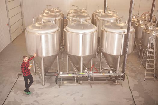Professional brewer standing near beer tanks rows at his beer factory, copy space
