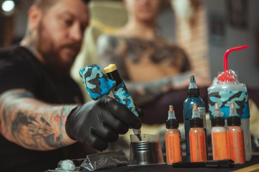 Selective focus on tattoo ink on the foreground, tattooist refilling the pen, while making tattoo for his client. Professional tattoo artist working at his studio. Man getting chest tattoo. Tattooing concept