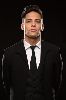 Vertical studio portrait of a handsome young secret service agent wearing black suit and a tie posing fiercely and confidently on black background safety bodyguard profession masculinity fearless