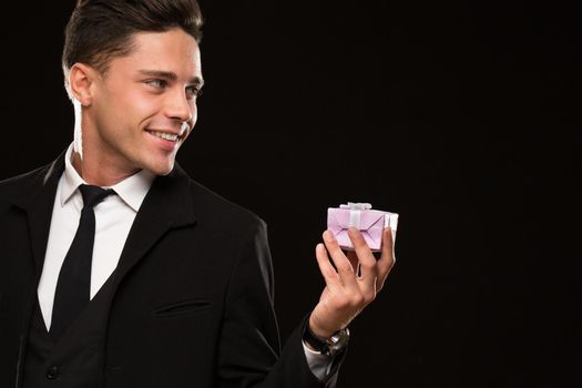 Cropped close up of a handsome young man in a black suit smiling happily holding a present looking at the copyspace celebration festive romance love relationships surprise dating gift flirt