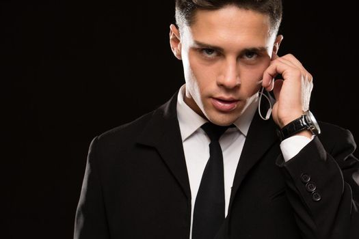 Close up of a handsome young suited secret service agent looking to the camera fiercely talking on his earphones black background copyspace infrmation security guarding bodyguard FBI secrecy