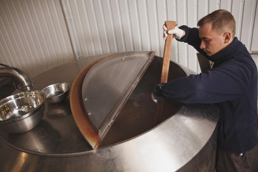 Brewer mixing beer in brewing tank, copy space