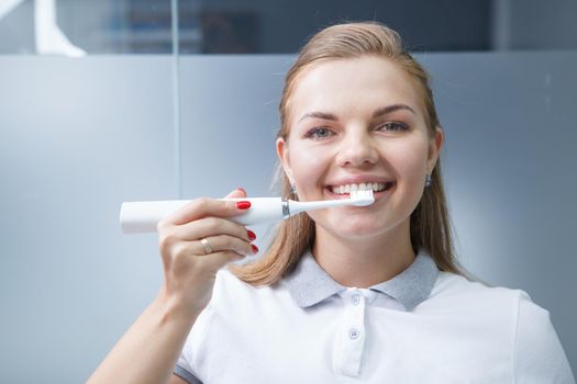 Happy beautiful female dentist smiling, holding up electric toothbrush to her teeth