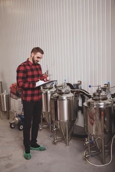 Vertical full length shot of a brewerwriting on his clipboard, working at his microbrewery