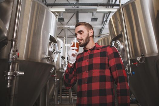 Low angle shot of a bearded handsome brewer smelling delicious beer, working at his microbrewery