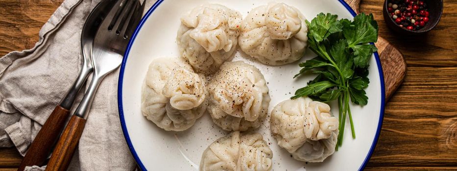 Khinkali, traditional dish of Georgian Caucasian cuisine, dumplings filled with ground meat on white plate with herbs on wooden rustic background table top view.