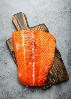 Top view, close-up of whole  fresh raw salmon fillet with seasonings on wooden board, gray stone background. Preparing salmon fillet for cooking, healthy eating concept