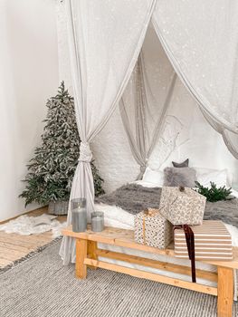 Christmas decorated rustic wooden bedroom interior in gray, white, silver colours with big baldaquin bed, fake fur blanket, candles, Christmas fir tree and gifts on floor. Christmas morning.