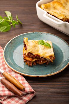 Slice of homemade traditional Italian lasagna with beef bolognese ragout and cheese served on blue ceramic plate on dark brown rustic wooden table, angle view