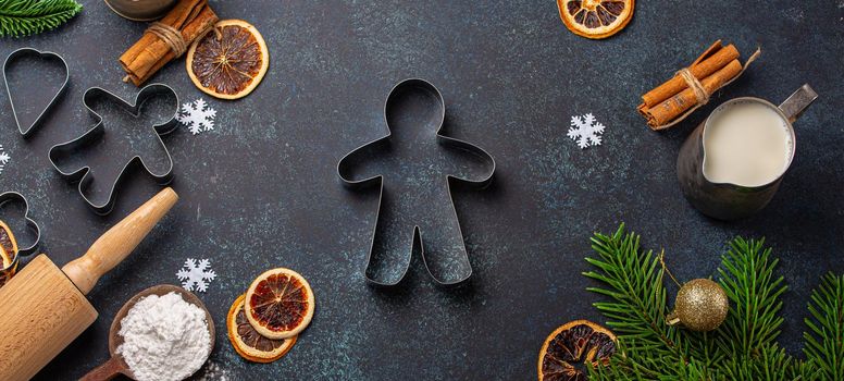 Christmas and New Year baking composition with kitchen tools, flour, milk, balls, fir tree and gingerbread man cutter in center on dark blue stone concrete background table top view