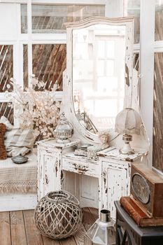 White vintage dressing table with retro lamp, antique vases, dried flowers in light shabby chic vintage french Provence country interior room with wooden parquet and painted furniture.