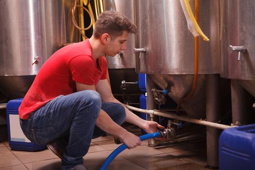 Young male brewer connecting a hose to metal tank at the brewery