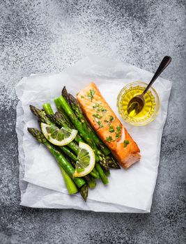 Grilled salmon fillet with green asparagus and seasonings, gray concrete background. Healthy balanced meal with salmon and asparagus good for diet and wellness, top view, close-up