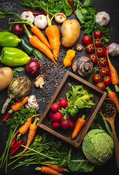 Radish and carrot fresh bunch in old wooden box and fresh farm organic vegetables on rustic black concrete background. Autumn harvest, vegetarian food or clean healthy eating concept, top view