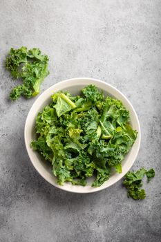 Bowl of fresh green chopped kale on gray rustic stone background, top view, close-up. Ingredient for making healthy salad. Clean eating, detox or diet concept