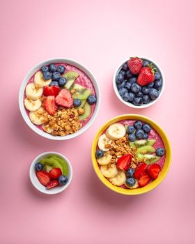 Two Summer acai smoothie bowls with strawberries, banana, blueberries, kiwi fruit and granola on pastel pink background. Breakfast bowl with fruit and cereal, close-up, top view, healthy food