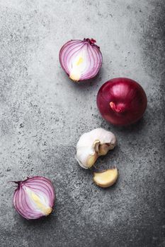 Close-up, top view of cut raw fresh red onions and garlic on rustic gray stone background. Cooking, vegetarian food or healthy eating concept, clean organic food