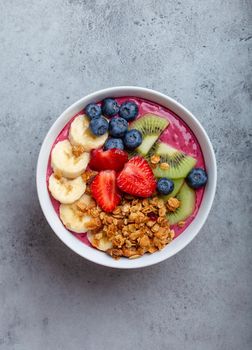 Two summer acai smoothie bowls with strawberries, banana, blueberries, kiwi fruit and granola on gray concrete background. Breakfast bowl with fruit and cereal, close-up, top view, healthy food